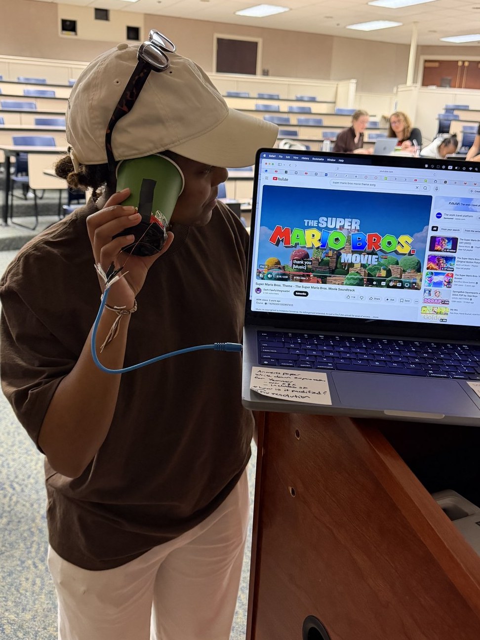 A student testing a headphone they built from a cup, magnet, and wire during a physics lab